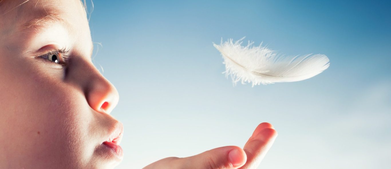 Ein Kind bläst sanft eine Feder in den Himmel. FederKraft wird spürbar.