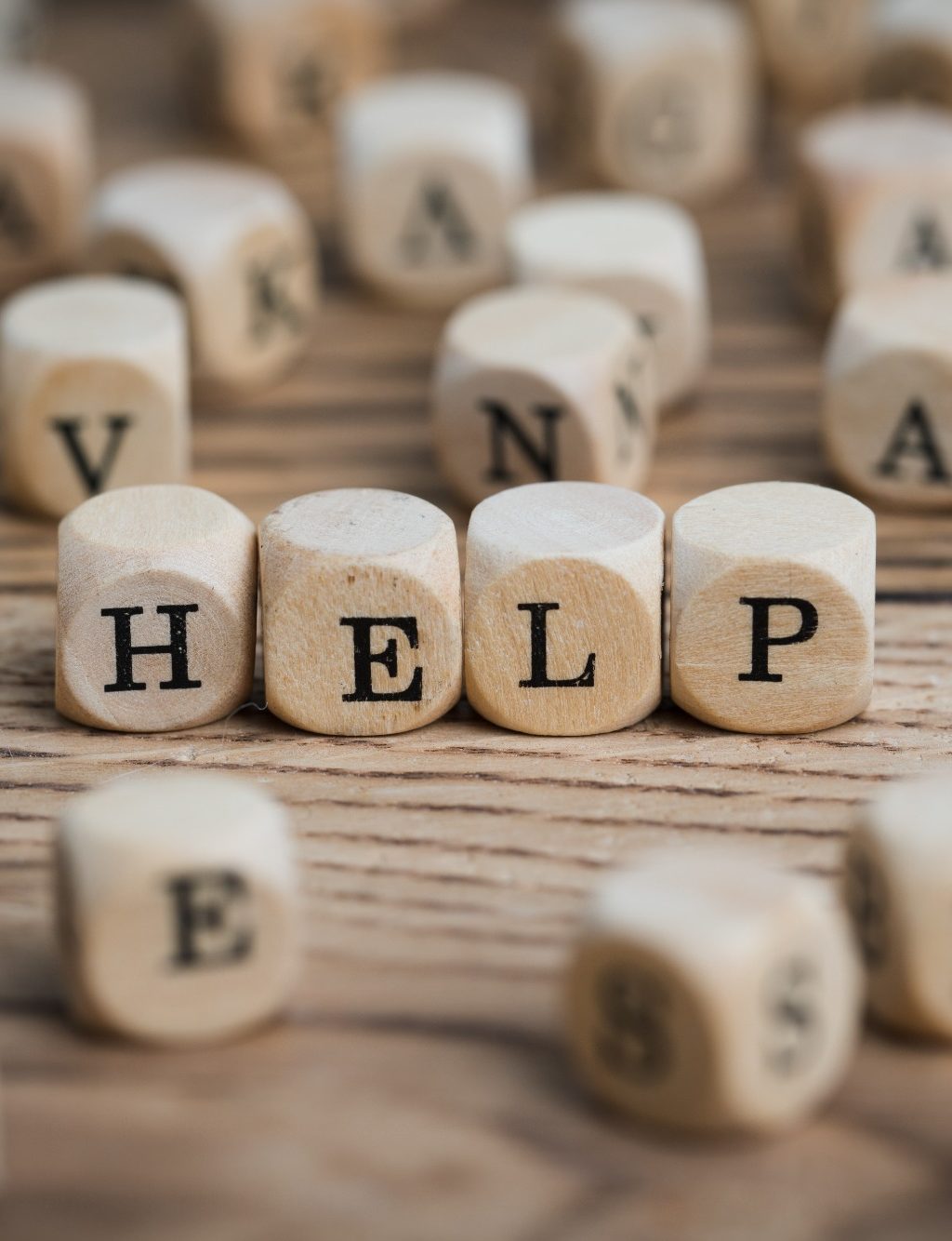 Buchstabenwürfel zeigen das Wort "HELP" auf einem Holzuntergrund.